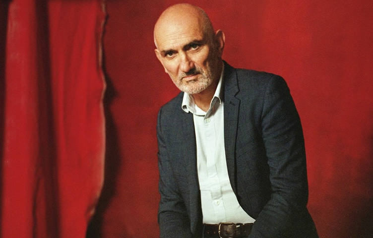 Paul Kelly wears a suit against a red background