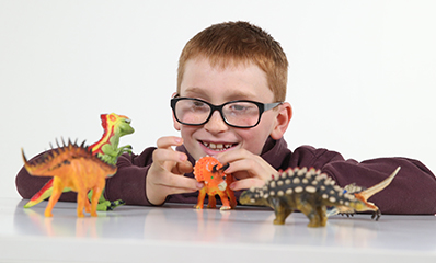 Young boy with glasses playing with toy dinosaurs