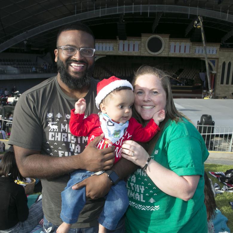 photo of man, woman and baby standing in front of the Carols stage looking happy