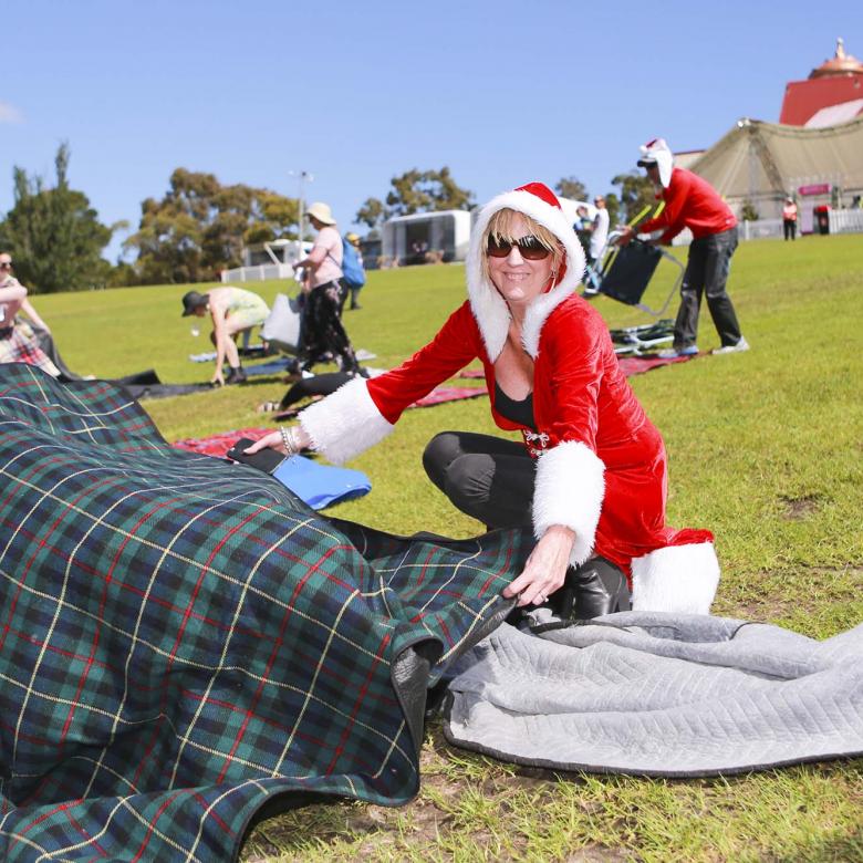 photo of a Carols guest wearing red sitting on a picnic blanket on the grass looking happy