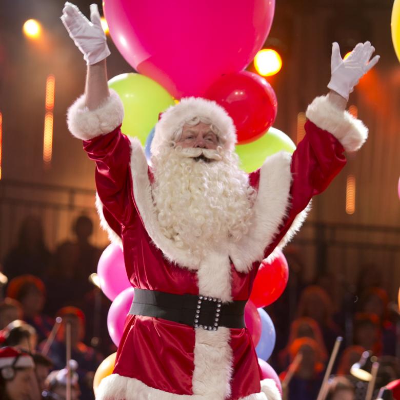 Photo of Santa on the Carols stage with his arms in the air during a performance