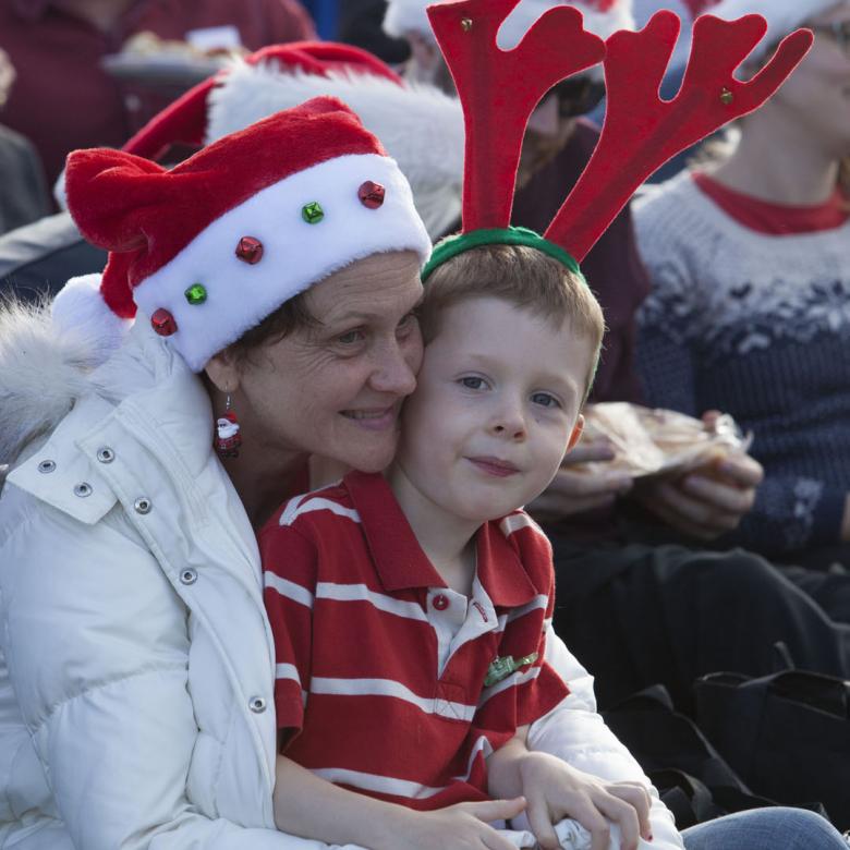 photo of a young boy sitting on the lap of a woman. He is wearing a headband with antlers on and she is wearing a santa hat