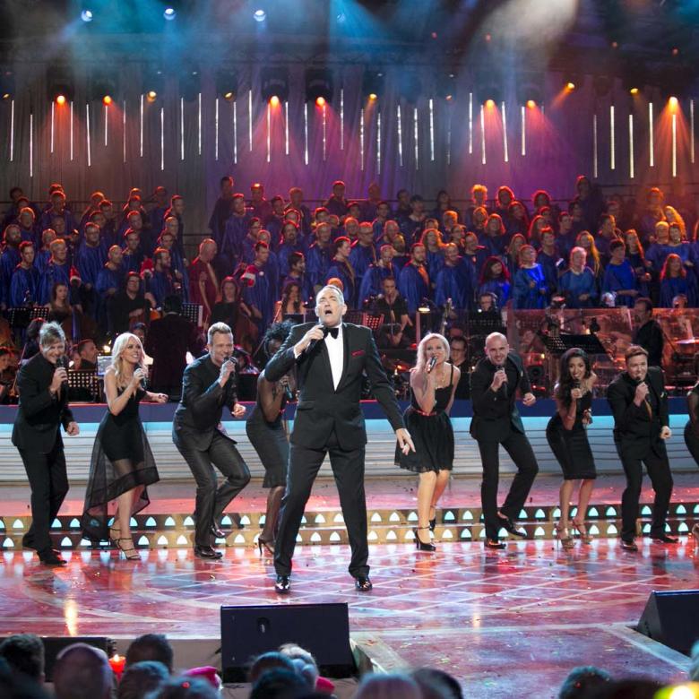 Photo of the Carols stage during a performance by Darren Percival wearing a black suit and the Melbourne Gospel Choir wearing black suits and dresses