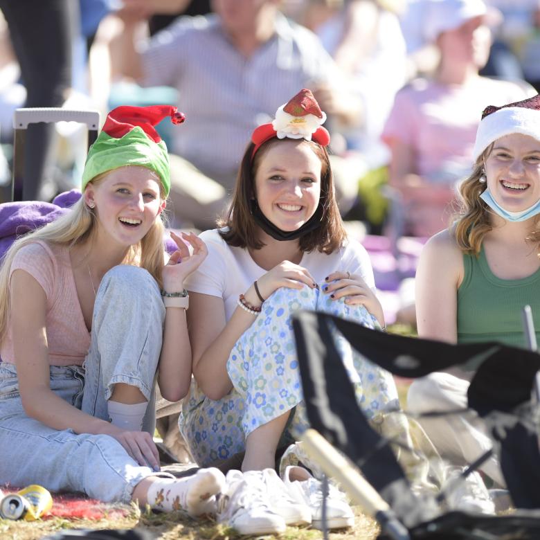Three girls in Christmas hats sit on a blanket on the lawn