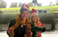 Rob Mills and Silvie Paladino on the stage of the Sidney Myer Music Bowl wearing tinsel and Santa hats