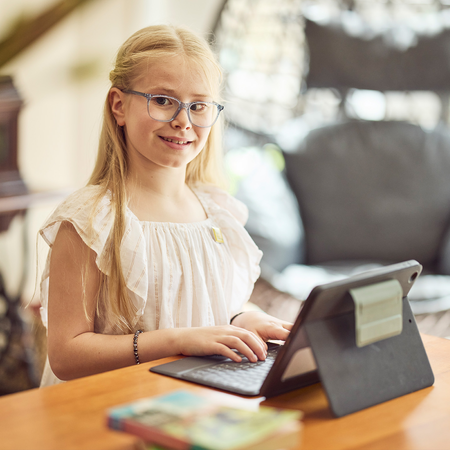 Young girl with blond hair and glasses sits at a table typing on a laptop