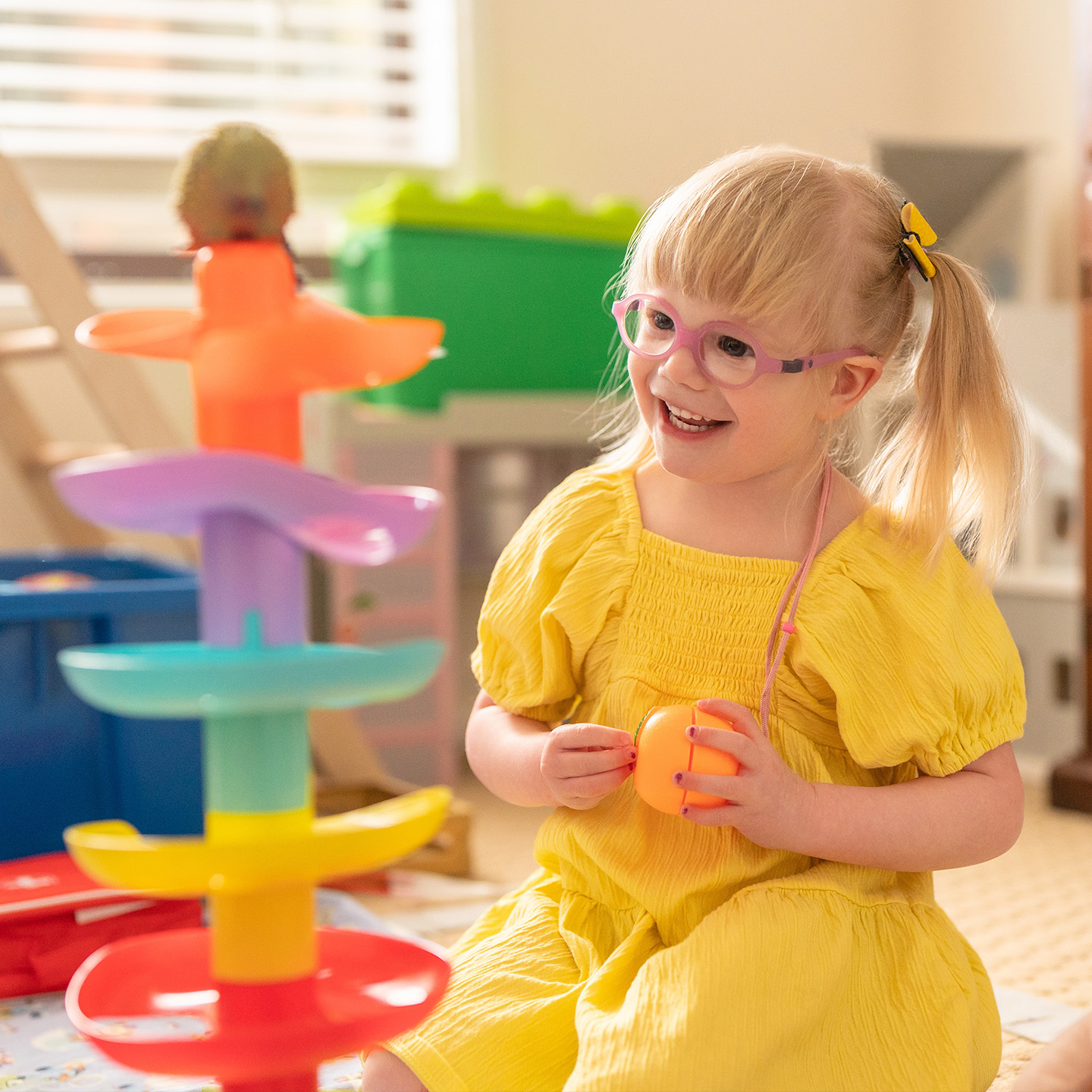Toddler in a yellow dress plays with toys on the floor
