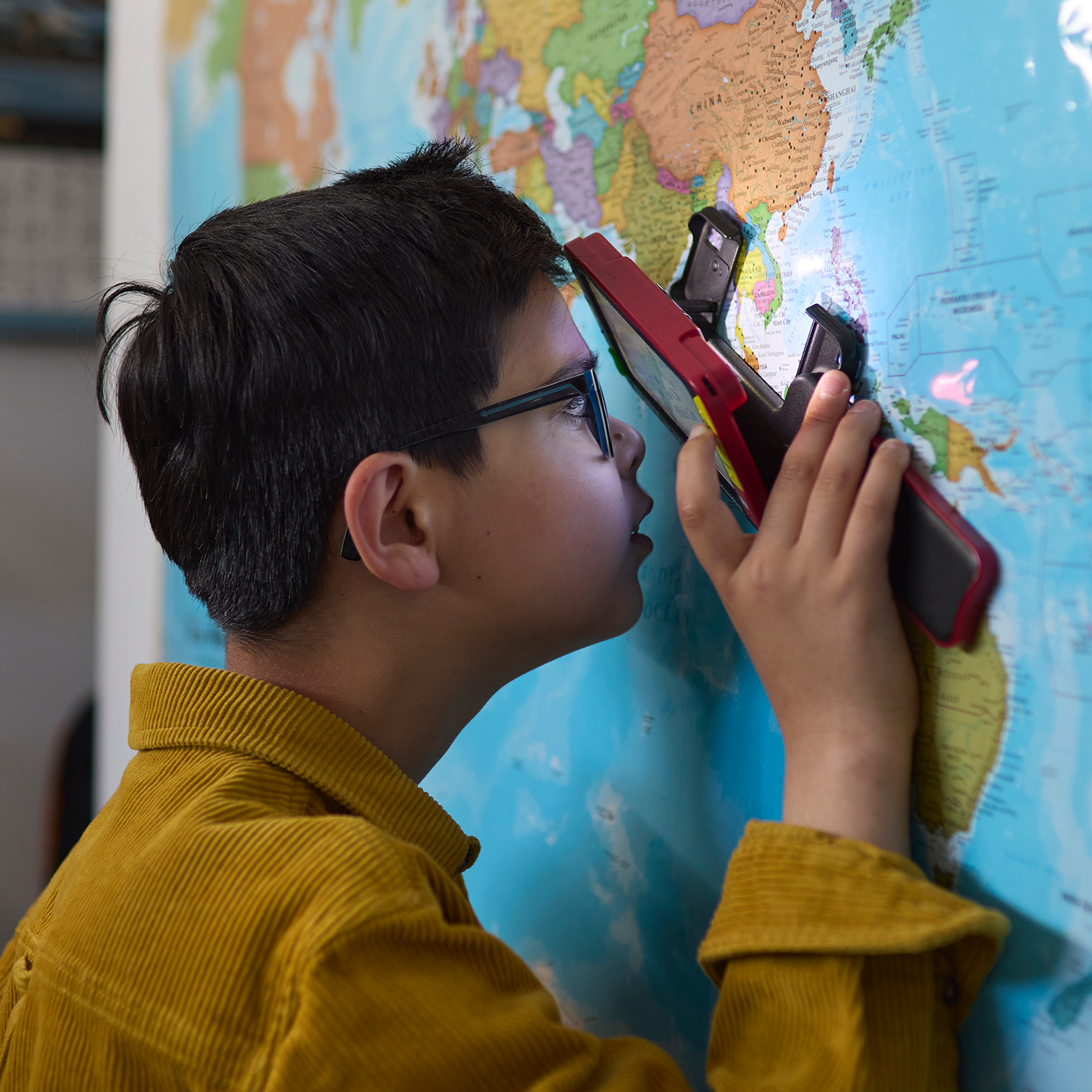 Mikail looks through a magnifier at a world map