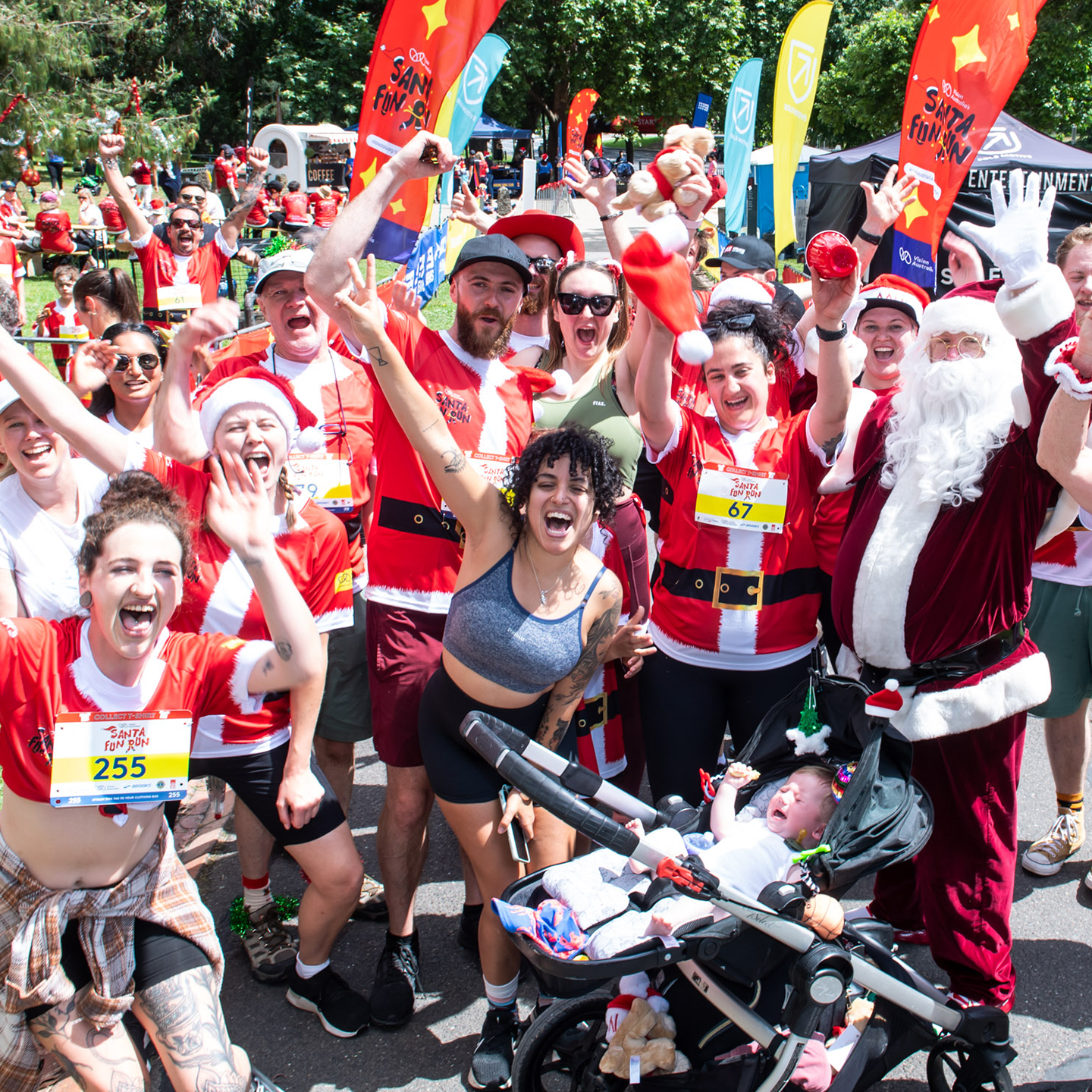 Group of people dressed in Santa Fun Run Tshirts, wearing race bibs, smiling with their hands in the air