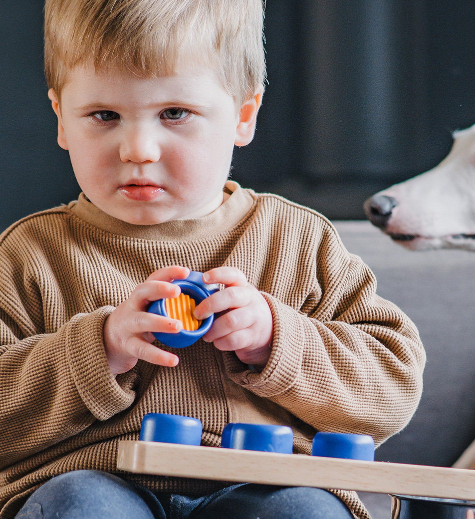 A young by sits looking to camera holding a block toy that sits on his lap
