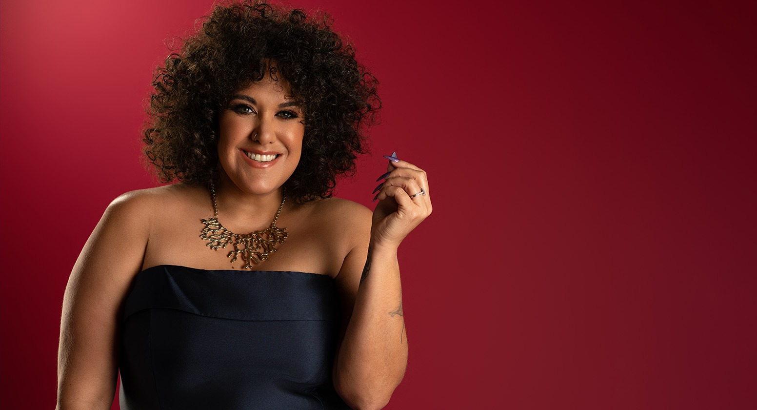 Casey Donovan wears a black dress against a red background