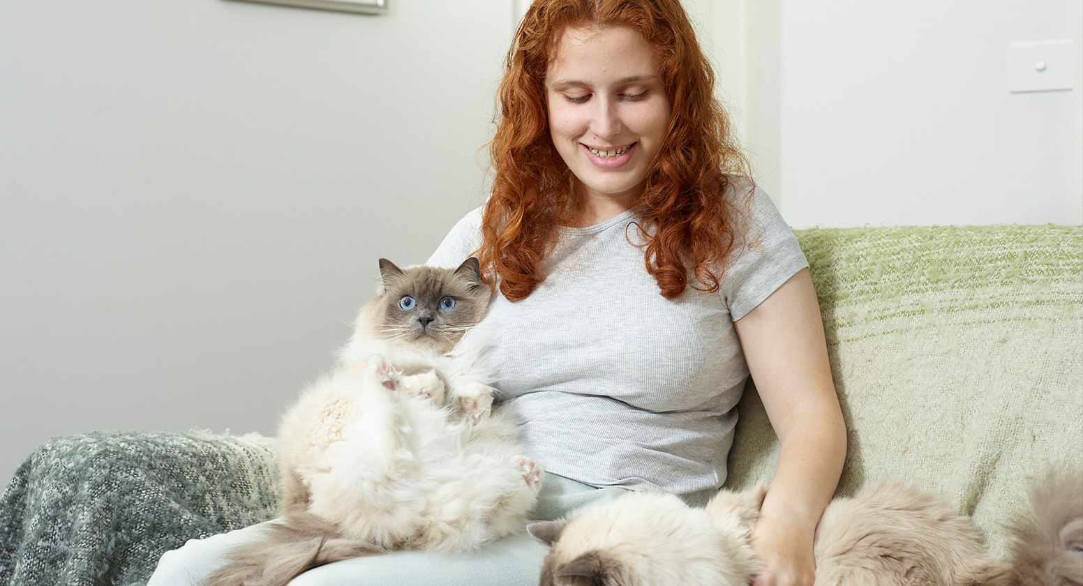 Lilly sits on a couch with her two cats