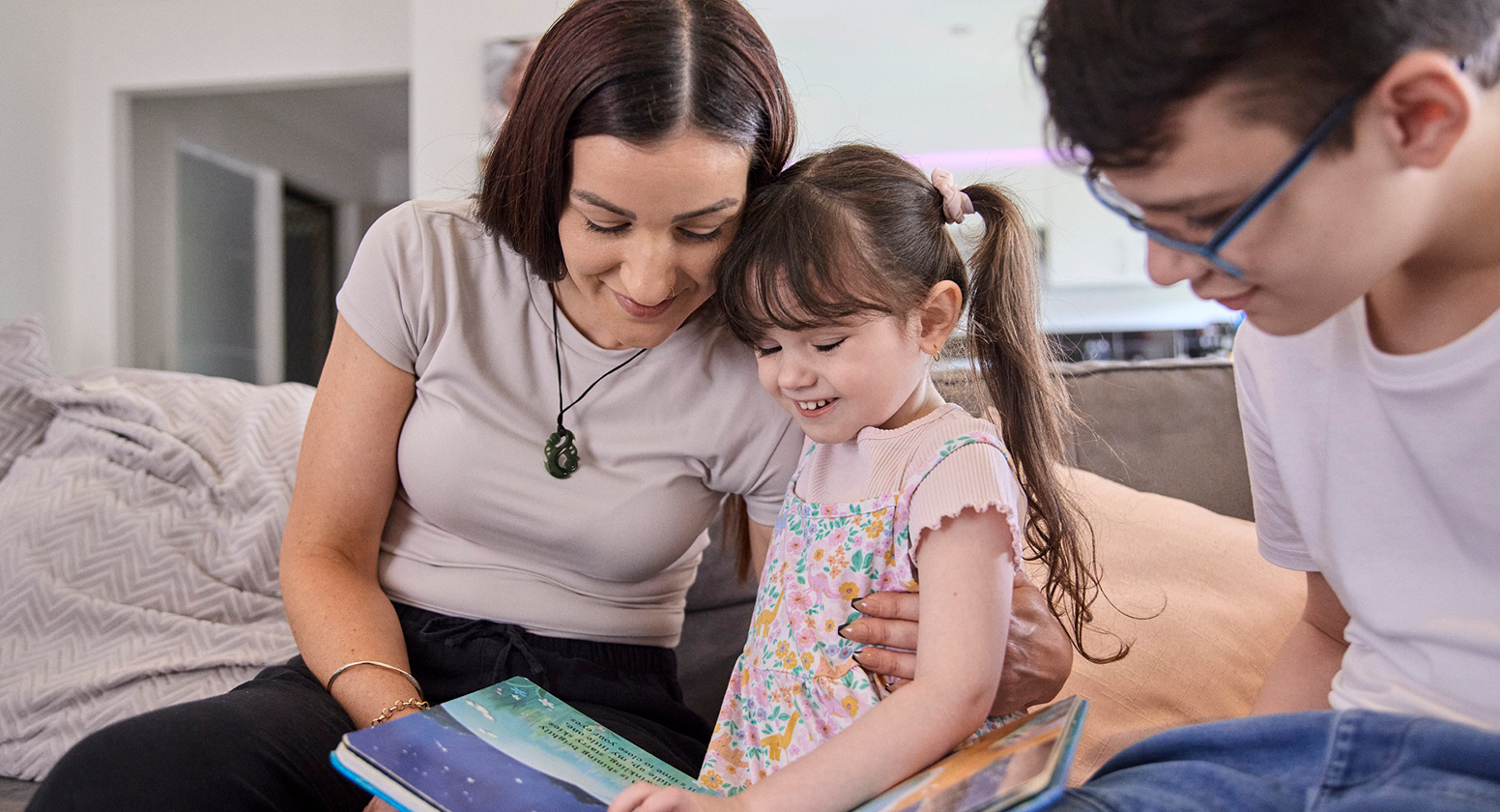 Marlee sits on the couch with her mum and brother reading a book