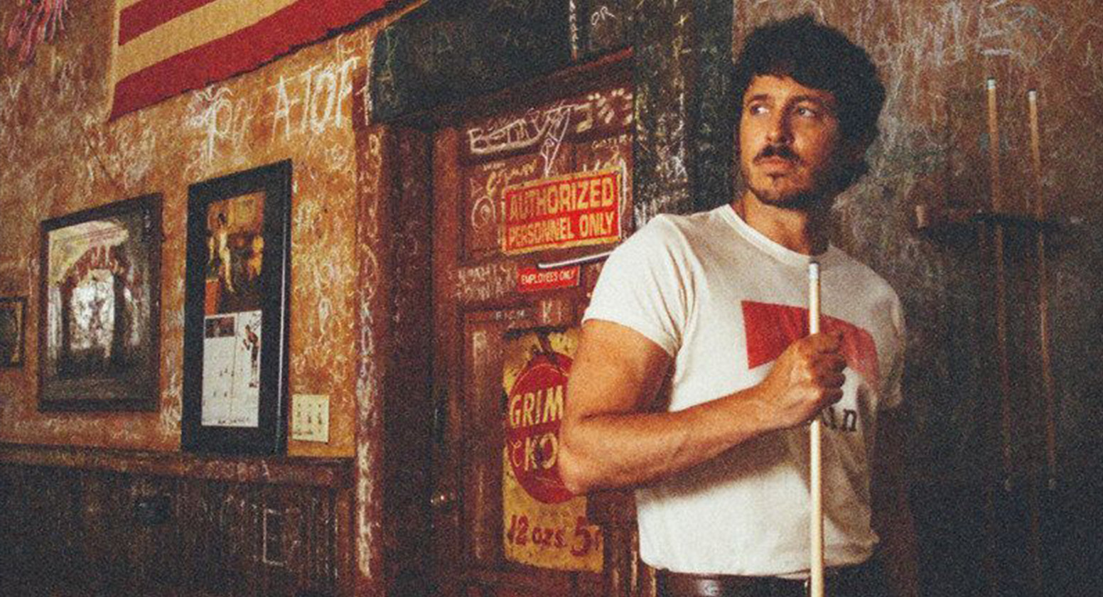 Morgan Evans against a rustic wall holding a pool cue