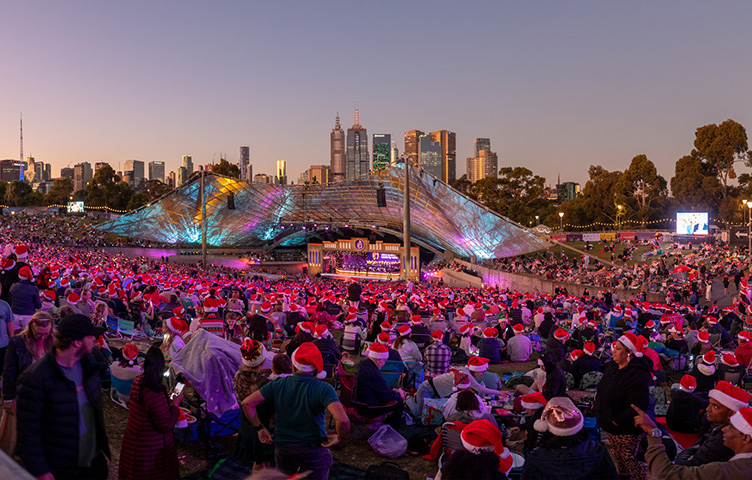 View of the Carols crowd from the back of the lawn showing the Sidney Myer Music Bowl and Melbourne skyline in the background