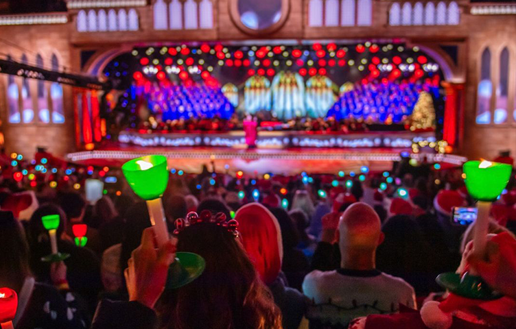 View of audience raising their candles up with the Carols by Candlelight stage in the background