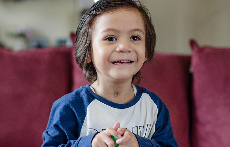 A young boy with dark hair smiles at the camera