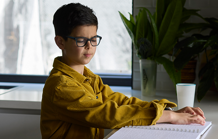 Mikail sits at a desk reading braille