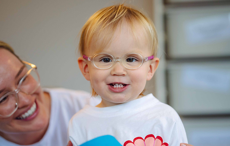 Young girl with blonde hair and glasses smiles at the camera