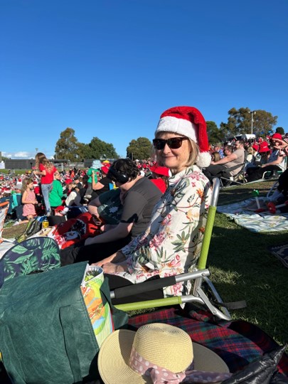 Woman wearing a Santa hat sits on a low deck chair in the Carosl by Candlelight crowd