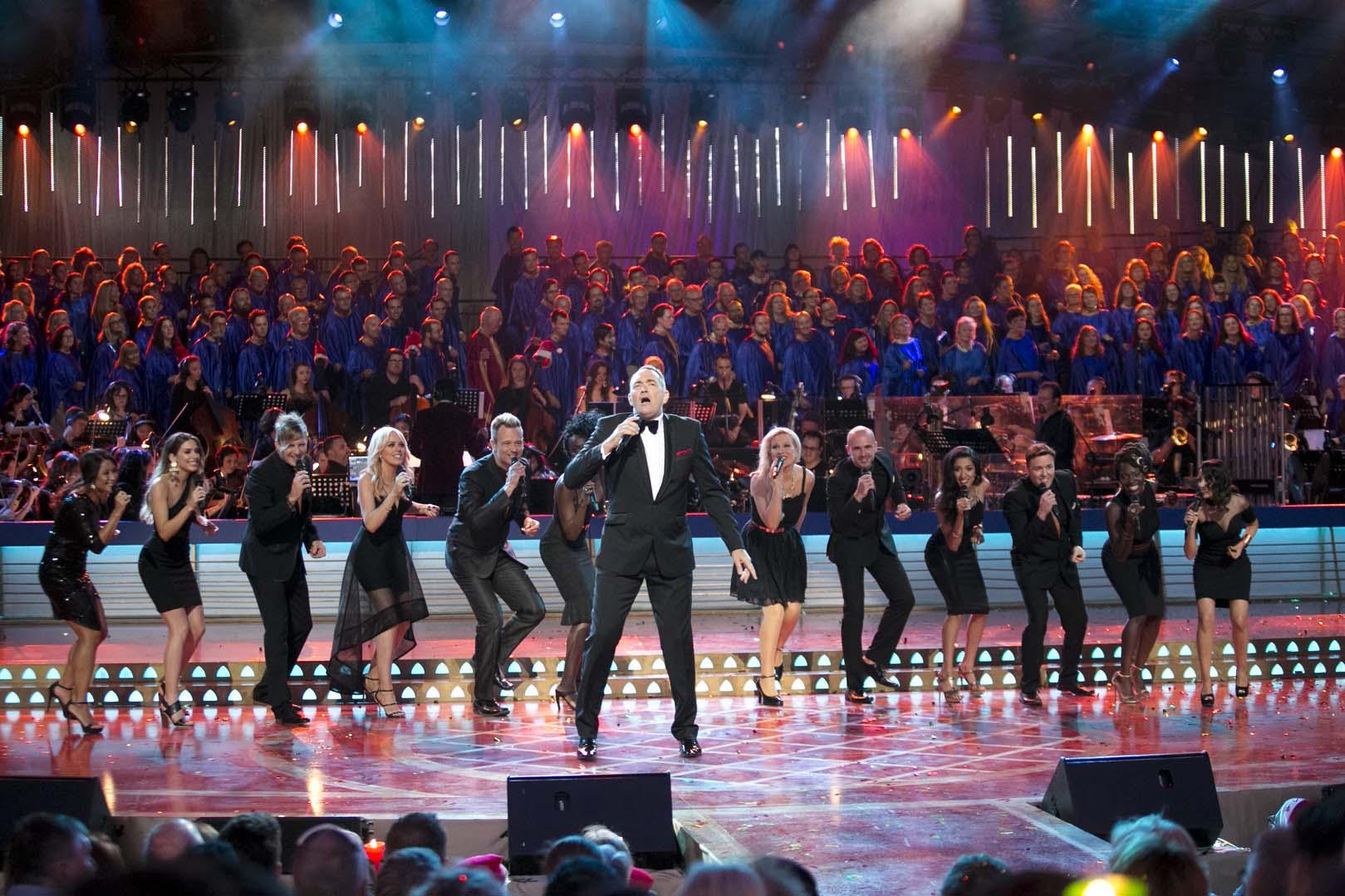Darren Percival performs on stage wearing a black suit and the Melbourne Gospel Choir wearing black suits and dresses