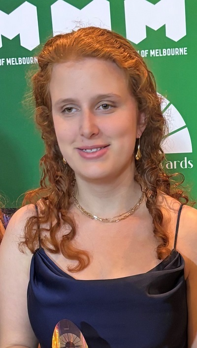 Young woman wearing a blue satin top stands in front of a green background smiling