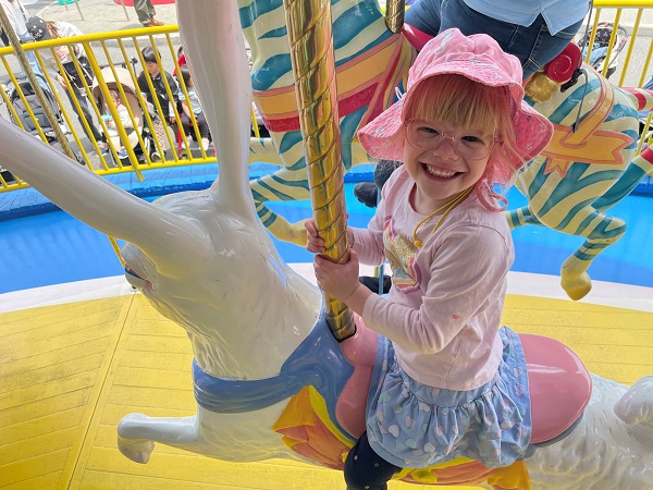 Young blonde girl sits smiling on a carousel